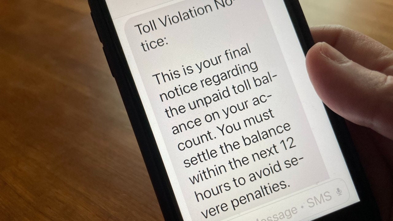 A person holds a cell phone with a text scam notification on it about a toll violation.