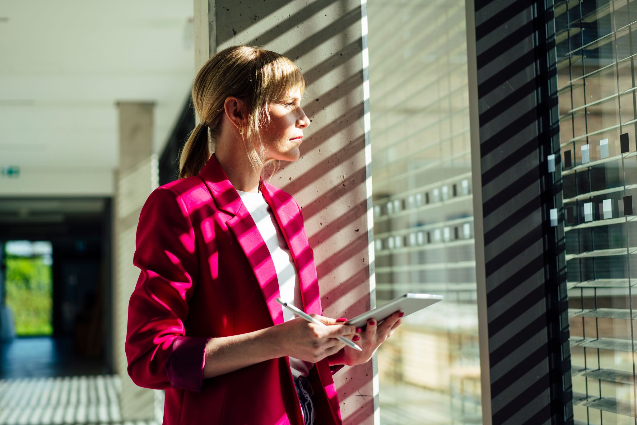 2484931583 Thoughtful blond businesswoman with tablet pc standing by window at office