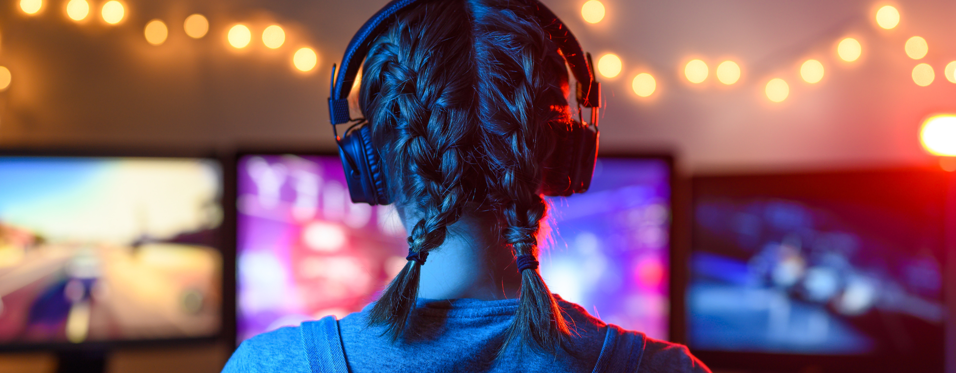 Photo of the back of a female gamer's head. She is wearing headphones and facing three computer screens.