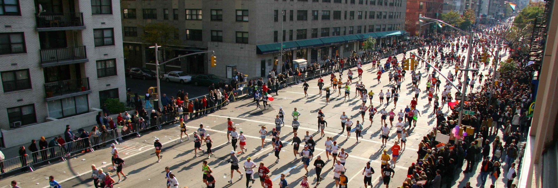 Runners in the New York City Marathon stream down a city street with people cheering on the sidelines.