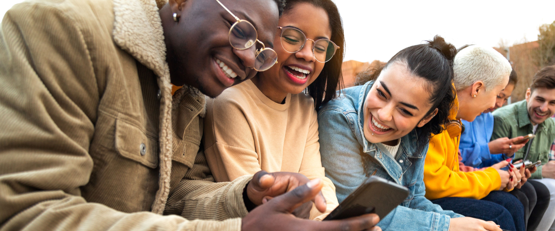 Happy young people looking at a mobile phone together outdoors. 