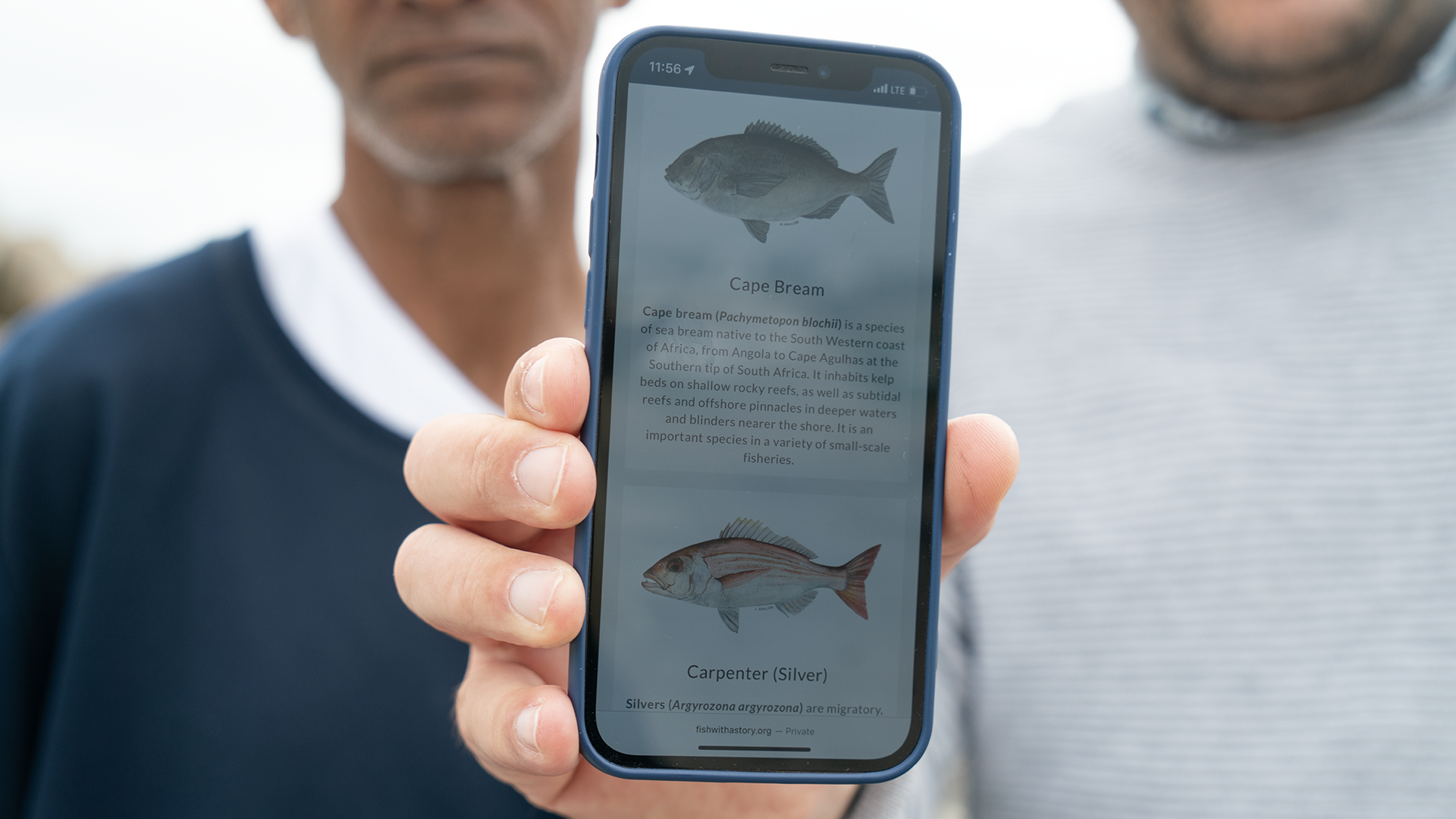 A fisherman holds up a phone that shows information about different species of fish.