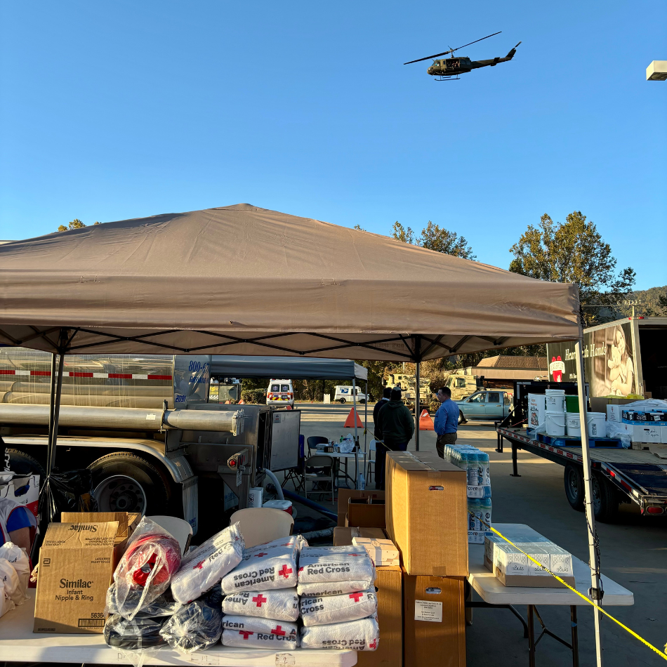 A tent set up at a Red Cross community care center with supplies for Hurricane Helene victims. A helicopter flies overhead. 