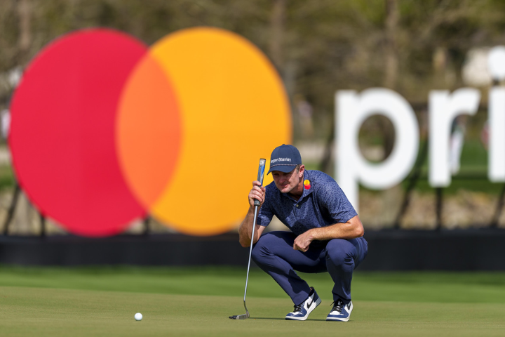 Justin Rose kneels on the green in front of a Mastercard logo. 