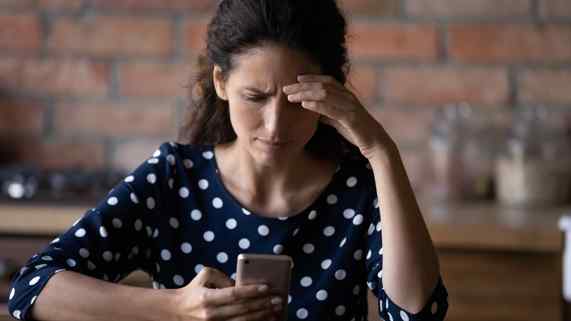 A woman looks down at her smartphone with a worried expression.