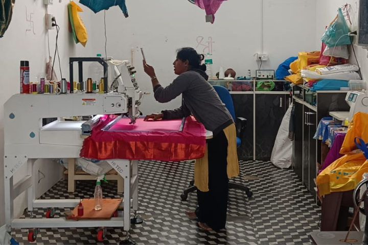 Sweta YM stands over a swath of pink fabric in her embroidery shop.